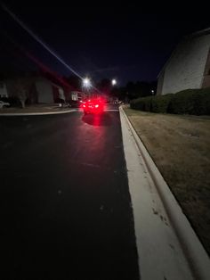 a red car is parked on the side of the road at night with its lights on