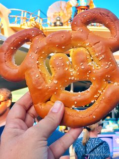 someone is holding up a pretzel shaped like mickey mouse at the amusement park