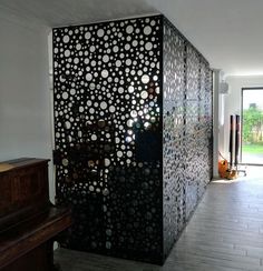 a room divider made out of metal circles and holes on the wall, with a piano in the foreground