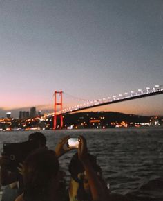 people taking pictures with their cell phones in front of the golden gate bridge at night