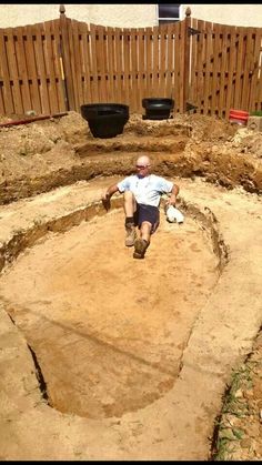 a man laying on top of a dirt field next to a wooden fence in the middle of a yard