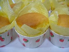 four muffins in paper cups with strawberries on the bottom and yellow wrappers around them