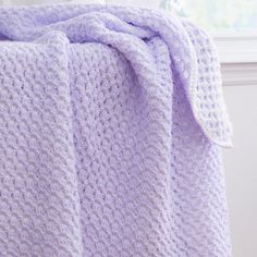 a purple crocheted blanket sitting on top of a bed next to a window