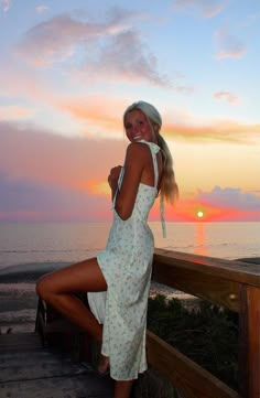 a woman in a white dress and hat posing on a wooden deck near the ocean