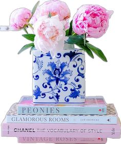 three pink peonies in a blue and white vase on top of four books