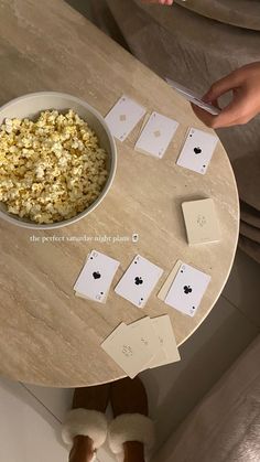 a table topped with cards and a bowl of popcorn next to two people's feet