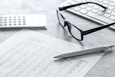 a pen, glasses and calculator sitting on top of a paper next to a keyboard