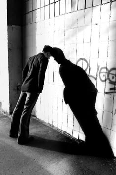 a man leaning against a wall with his hand on the back of another person's head