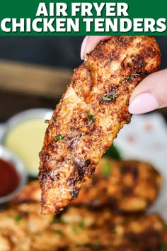 a hand holding up a piece of chicken tenders over a plate of fried food