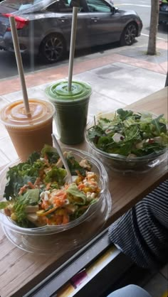 two salads and drinks sit on a table in front of a window with cars