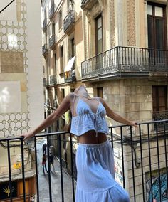 a woman in a blue dress is standing on a balcony with her arms spread out