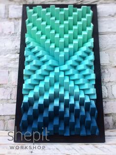 an art piece made out of blue and green squares on a black frame with brick wall in the background