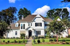 a large white house with lots of trees in the front yard and landscaping around it