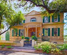 an old house with green shutters and trees on the side walk in front of it