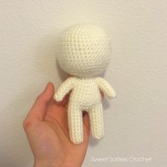 a hand holding a small white crocheted doll on top of a wall next to a white wall