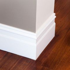 the corner of a room with wood flooring and white trim on the baseboard