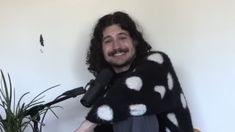 a man wearing a polka dot sweater and holding a microphone in front of a white wall