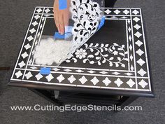 a person using a sponge to paint a table with black and white designs on it