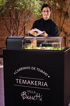 a man standing behind a counter that has food in it and the words temakeria written on it