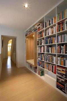 a room filled with lots of books on top of shelves next to a hallway leading to an open door