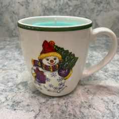 a white cup with a snowman on it and a candle in the middle is sitting on a counter