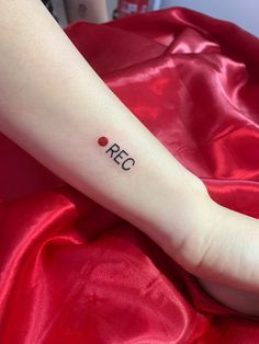 a person with a small red dot tattoo on their left arm and the word rec written in black ink