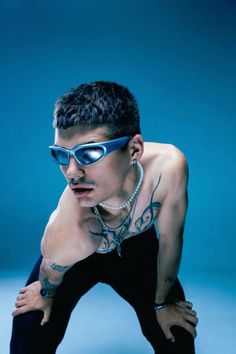 a man with tattoos and sunglasses on posing for a photo in front of a blue background