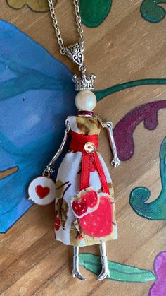 a necklace with a doll wearing a crown and holding a heart on it's back