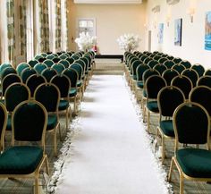 rows of green chairs with white flowers on them in a room filled with windows and drapes