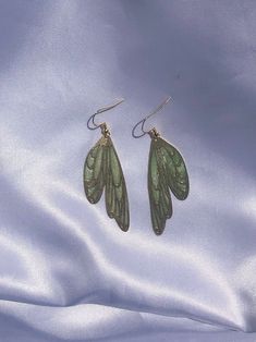 Shimmery pastel green resin in a brass wing shaped setting. Golden hypoallergenic earring hooks are made of 925 silver-plated copper. Each piece is handmade and is created by carefully pouring and mixing resin into each individual section. This tedious process leads to beautiful vibrant colors that imitate a stained glass look in a much more durable and lightweight way. Every piece is naturally unique as it is impossible to maintain the pigment to resin ratio, leading to large variations of colo Green Fairy Earrings For Gift, Fairy Style Green Earrings For Gifts, Handmade Green Fairy Jewelry, Green Hypoallergenic Brass Earrings, Hypoallergenic Green Brass Earrings, Green Moth, Green Fairy Wings, Fairy Wing Earrings, Magnolia Garland