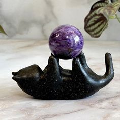 a purple marble ball sitting on top of a black elephant figurine with it's head in the air