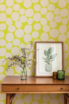 a wooden table topped with a vase filled with flowers next to a wallpapered wall