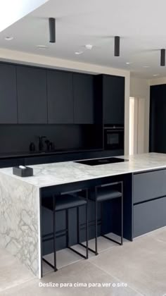 a kitchen with black cabinets and marble counter tops in the center is an island that has stools on it