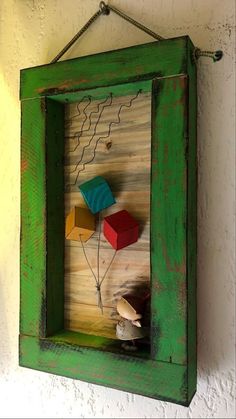 a green frame with some colorful items in it hanging on the side of a wall