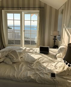 an unmade bed sitting in front of a window with a laptop on top of it