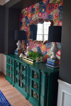 a room with a green dresser and colorful wallpaper