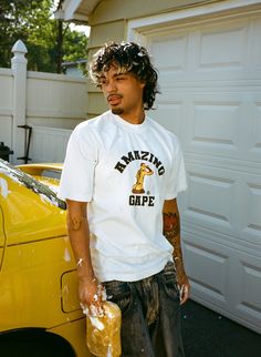 a man standing next to a yellow car holding something in his hand and looking at the camera