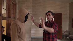 two men standing in a room with one wearing a hoodie and the other holding his hands out