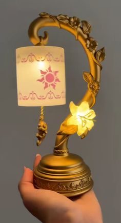 a hand holding a lamp with a flower on it and the light is turned on