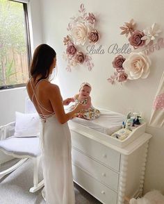 a woman standing next to a baby in a crib with flowers on the wall