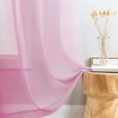 a pink sheer curtain hanging over a wooden table next to a vase with dry grass in it