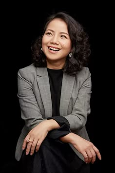 a woman in a gray jacket and black shirt sitting on a chair with her arms crossed