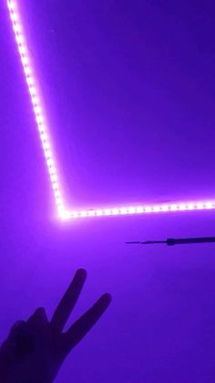 a person holding up their hand in front of a purple wall with lights on it