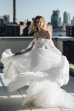 a woman in a white dress is walking down the sidewalk with her long flowing skirt