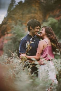 a man and woman are standing in tall grass with their arms around each other as they look into the distance