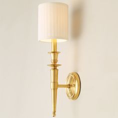 a gold wall light with a white shade on it's side and a lamp attached to the wall