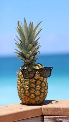 a pineapple with sunglasses sitting on a ledge next to the ocean in front of it