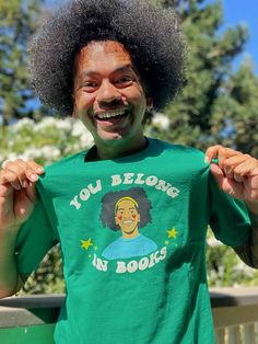 a man with an afro holding up a t - shirt that says you belong in books