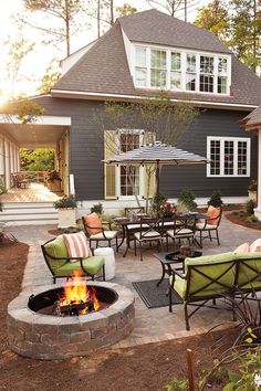 an outdoor patio with chairs, tables and fire pit in front of a gray house