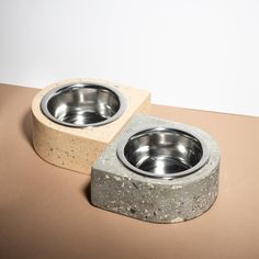 two cement bowls sitting on top of a brown table next to each other with one bowl in the middle